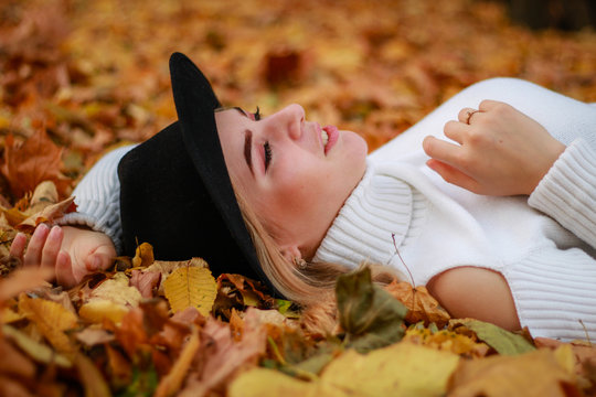 Autumn girl portraits. Model in white sweater lies on yellow leaf. Black hat. Bright eyes. Atmospheric photos.