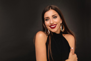 Close up portrait of smiling caucasian woman with holiday make up smiling to camera wearing gold earnings and black blouse 