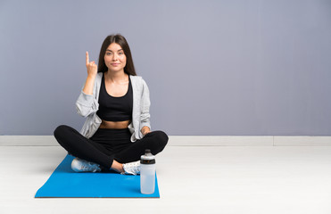 Obraz premium Young sport woman sitting on the floor with mat pointing with the index finger a great idea