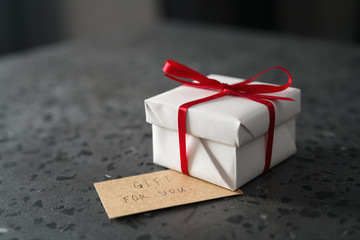White gift box with red ribbon and paper card on terrazzo surface