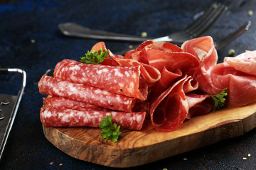 Food tray with delicious salami, coppa, crudo and herbs. Meat platter with selection on rustic table