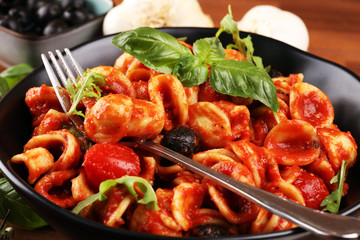 Pasta orecchiette. Plate of delicious orecchiette with tomato sauce garnished with parmesan cheese and basil on rustic background