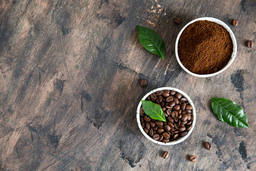 coffee beans and ground coffee in bowls with coffee tree leaf on a dark background. copy space for your text