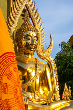 The golden Buddha face and the Buddhist yellow flag in outdoor of the temple in Thailand with the blue sky copy space