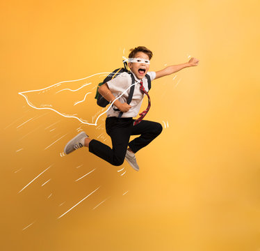 Young boy student jumps high like a super hero. Yellow background