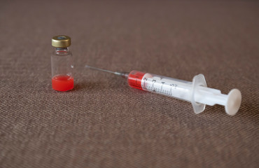 Closeup syringe and bottle with red liquid in the fabric surface