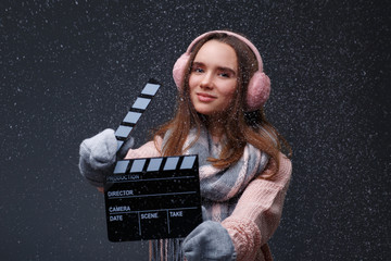 Young beautiful smiling girl in knitting pullover holding director's clapper board for making...