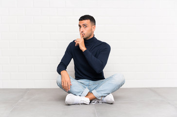 Young handsome man sitting on the floor doing silence gesture
