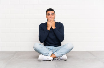 Young handsome man sitting on the floor with surprise facial expression