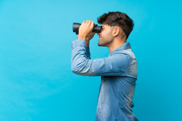 Fototapeta premium Young handsome man over isolated blue background with black binoculars