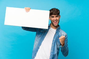Young handsome man over isolated blue background holding an empty white placard for insert a concept