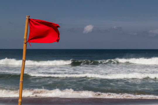 Red Warning Flag Flapping In The Wind On Beach At Stormy Weather.