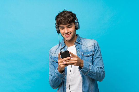Young handsome man over isolated blue background using the mobile with headphones