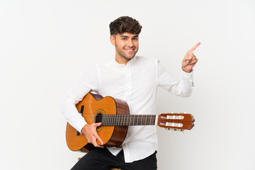 Young handsome man with guitar over isolated white background surprised and pointing finger to the side