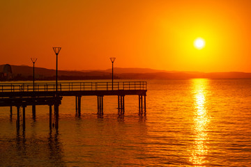 Fototapeta na wymiar Island of Cyprus. Sunset over the Mediterranean sea. View of the setting sun from the Limassol waterfront. Picturesque wharves on the background of orange sunset. Panorama Of Cyprus.