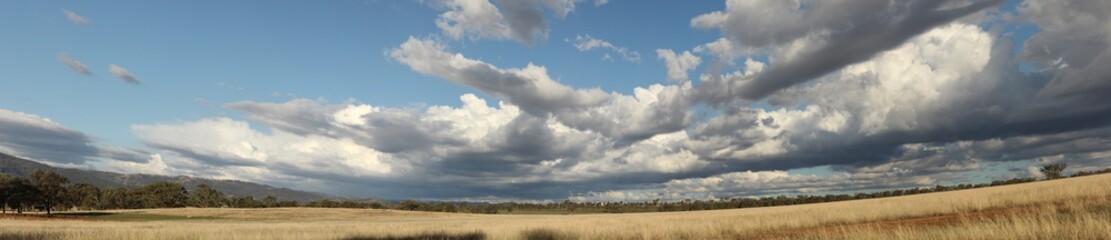 Panoramic view of large open dry drought affected farm fields under stretching cloud filled blue skies over properties in rural New South Wales, Australia