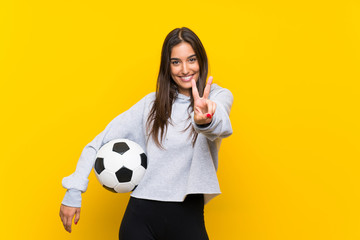 Young football player woman over isolated yellow background smiling and showing victory sign