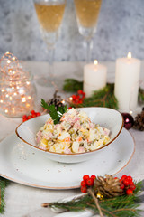 Festive salad with sausage, vegetables and mayonnaise. Christmas table setting with salad, Christmas decorations and garlands.