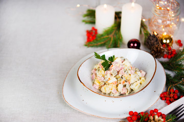 Festive salad with sausage, vegetables and mayonnaise. Christmas table setting with salad, Christmas decorations and garlands. Copy space