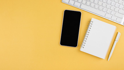 Flat lay design of modern office table with smartphone, laptop, notebook and pen on yellow background with copy space. Top view. Business, Workspace, learning and education concept.