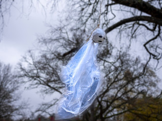 A cheap ghost made of plastic. Plastic ghot, made from blueish plastic hanging from a tree by the neck. 