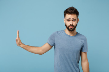 Young concerned man in casual clothes posing isolated on blue wall background, studio portrait. People sincere emotions lifestyle concept. Mock up copy space. Showing stop gesture aside with palm. - obrazy, fototapety, plakaty