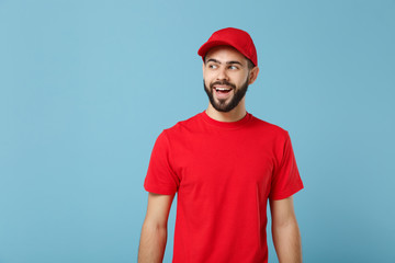Delivery man in red uniform workwear isolated on blue wall background, studio portrait. Professional male employee in cap t-shirt print working as courier dealer. Service concept. Mock up copy space.