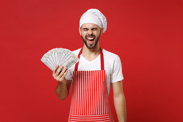 Screaming young bearded male chef cook or baker man in striped apron toque chefs hat isolated on red background. Cooking food concept. Mock up copy space. Hold fan of cash money in dollar banknotes.