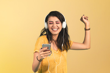 Young woman listening music with smartphone on yellow background