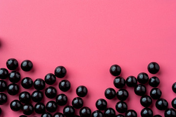 Close-up of black shiny pills lie on a pink surface