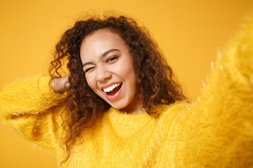 Close up of cheerful young african american girl in fur sweater posing isolated on yellow orange...
