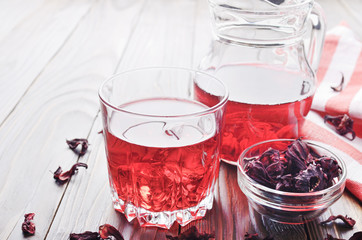 Closeup view at glass of hibiscus ice tea and jug on wooden table background