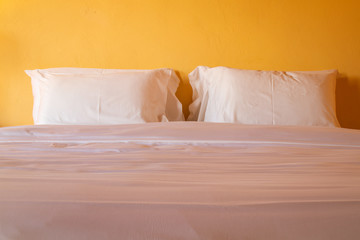 Fototapeta na wymiar White pillows on cozy bed in bedroom for interior decoration in warming light tone.