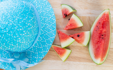 Slice watermelon and blue hat on the wooden pattern table background,