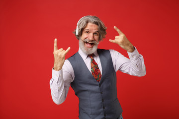 Elderly gray-haired mustache bearded man in shirt vest tie isolated on red wall background. People...