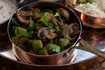 Indian okra and mushroom curry served in a copper plated serving pan
