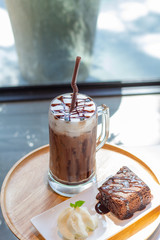Ice coffee a late art in the glass on the table background, chockolate cake in wooden tray,