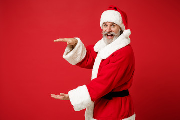 Elderly gray-haired bearded mustache Santa man in Christmas hat posing isolated on red background. New Year 2020 celebration concept. Mock up copy space. Demonstrating size with vertical workspace.