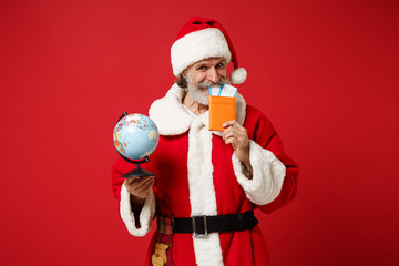 Fototapeta na wymiar Funny elderly gray-haired mustache bearded Santa man in Christmas hat posing isolated on red background. New Year 2020 celebration concept. Mock up copy space. Holding passport, ticket, world globe.