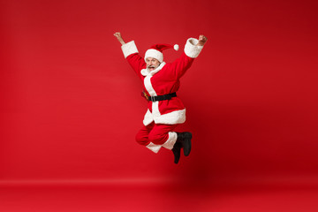 Funny elderly gray-haired mustache bearded Santa man in Christmas hat posing isolated on red wall...