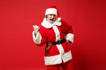 Fototapeta na wymiar Strong crazy elderly gray-haired mustache bearded Santa man in Christmas hat posing isolated on red background. Happy New Year 2020 celebration holiday concept. Mock up copy space. Holding dumbbells.