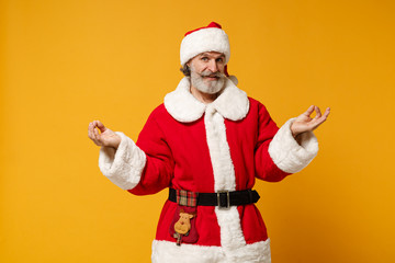 Fototapeta na wymiar Elderly gray-haired mustache bearded Santa man in Christmas hat posing isolated on yellow background. New Year 2020 celebration concept. Mock up copy space. Holding hands in yoga gesture, meditating.