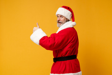 Fototapeta na wymiar Back rear view of elderly gray-haired Santa man in Christmas hat posing isolated on yellow background. New Year 2020 celebration holiday concept. Mock up copy space. Showing thumbs up, looking back.