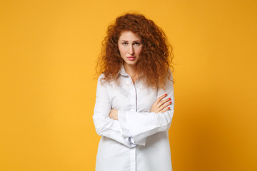 Displeased young redhead woman girl in casual white shirt posing isolated on yellow orange background in studio. People sincere emotions lifestyle concept. Mock up copy space. Holding hands crossed.