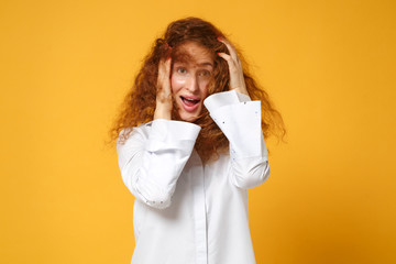 Excited young redhead woman girl in white shirt posing isolated on yellow orange wall background, studio portrait. People sincere emotions lifestyle concept. Mock up copy space. Putting hands on head.