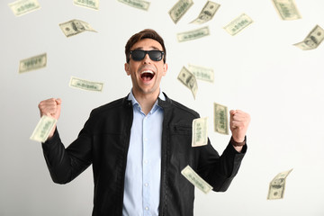 Happy young man and falling dollar banknotes on white background