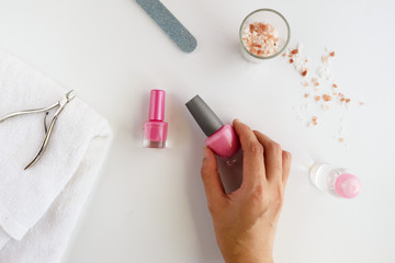 Woman having a manicure iat hpme with the nail tools product on white background, over head view of the hands.