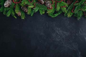 Christmas festive background with christmas tree branches, fir cones and red garland on dark concrete stone background.