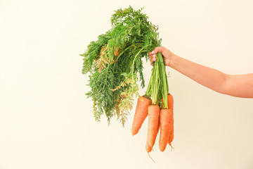 Female hand with fresh carrots on light background