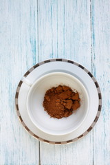 Brown vegetable carob (Ceratonia silica) for making a natural caffeine-free sweet drink. Dry carob powder in a white cup on a wooden background.
